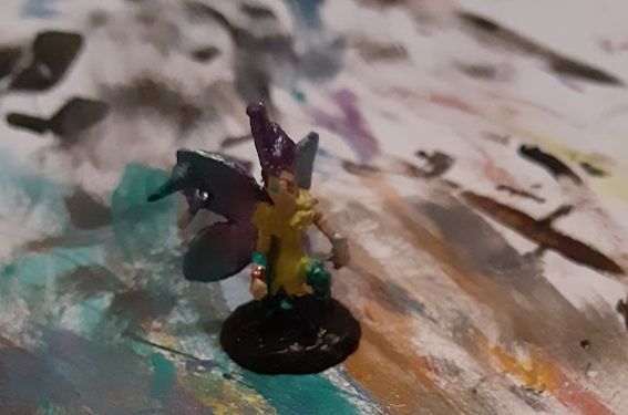 A mini figurine of a fairy, with a yellow dress and tall purple hair.