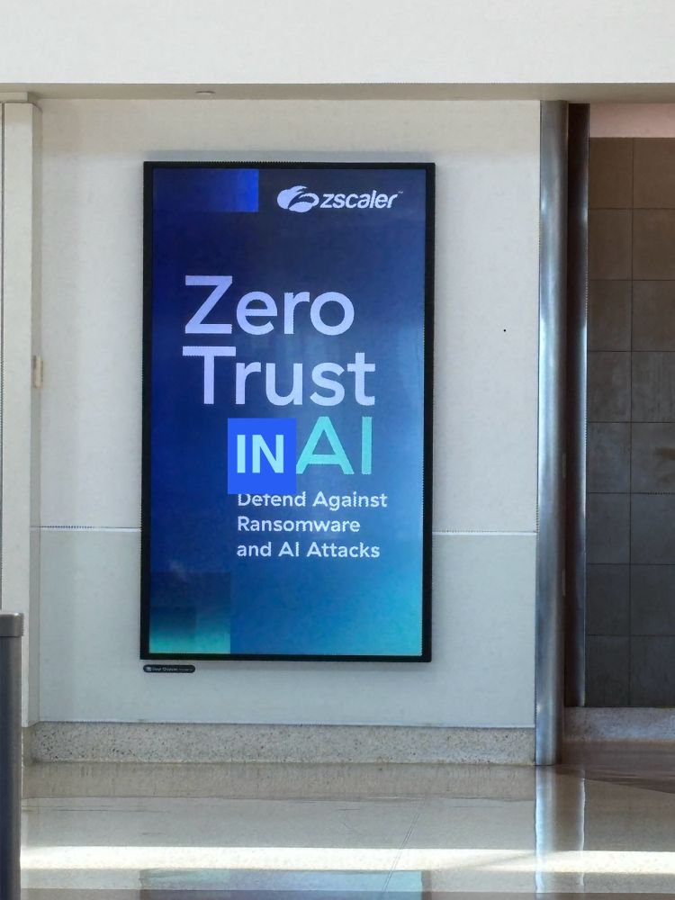 Photo of an ad which reads “Zero Trust + AI”, badly edited to say “Zero Trust IN AI” because we hate the plagiarism machine that lies.