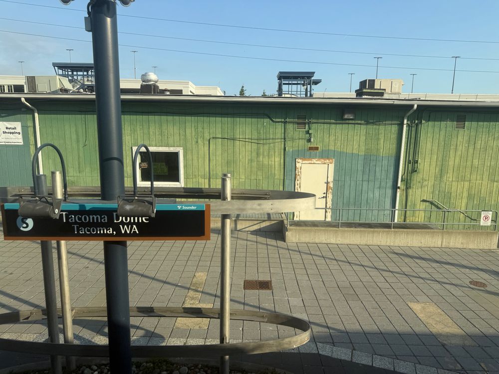 Picture of the Sounder Tacoma Dome station sign on the platform in front of an older green building