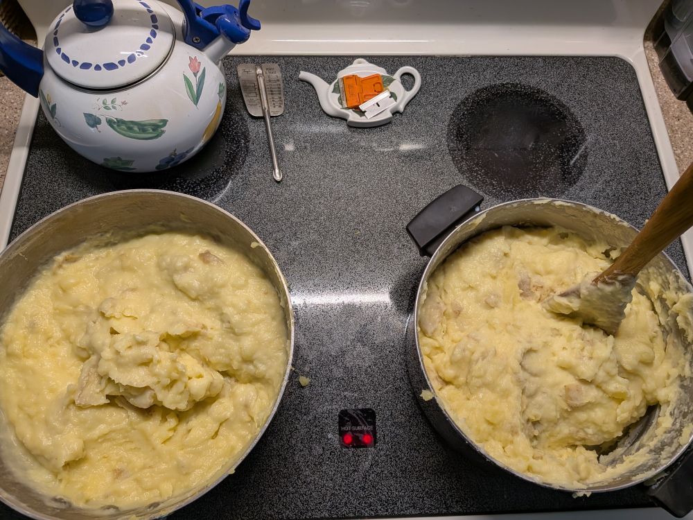 12 pounds of smoked Gouda mashed potatoes in two pots on a glass top stove.