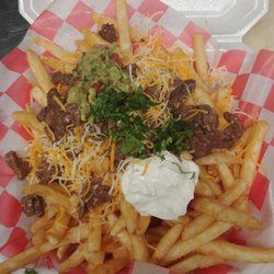 A Styrofoam to-go plate filled with Carne Asada Fries: French fries topped with shredded cheese, carne asada, sour cream, guacamole, and chopped cilantro. 