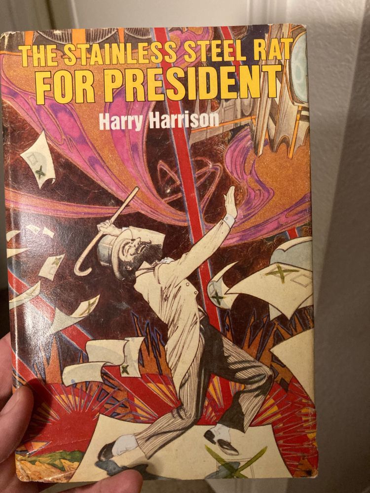 The Stainless Steel Rat for President by Henry Harrison. A bearded man, pure white, wears a suit and top hat and carries a cane, appearing to happily dance? In the foreground are what look to be single-issue ballots. The background is largely magenta, orange, and black, and it features a spaceship. 