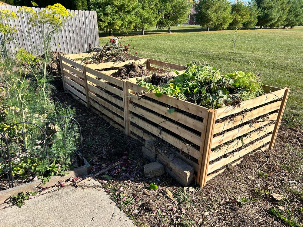 Three cedar composter fences in the back of a garden. 