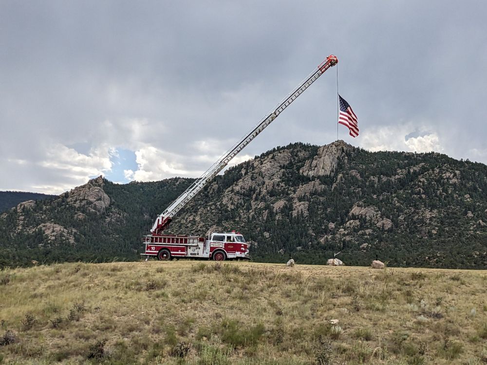 Fire truck hoisting a large American flag with mountains in the background