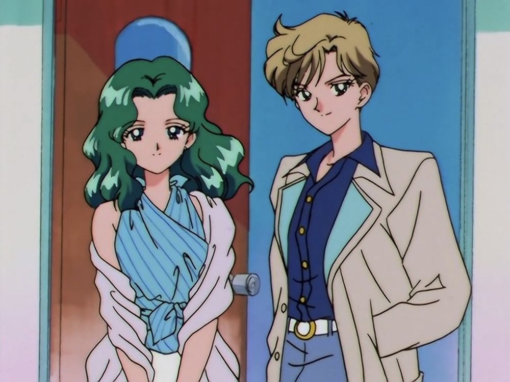 two characters standing side by side in front of a doorway. On the left, a character with long wavy green hair wears a blue striped halter-style top with a white wrap draped around their shoulders, and a soft expression. On the right, a character with short blond hair and a confident smile wears a navy blue shirt with a tan and aqua blazer, light blue pants, and a white belt.