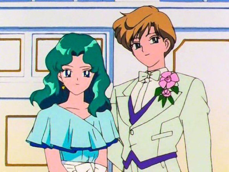 Two elegantly dressed characters standing side by side. The character on the left has long, wavy green hair and wears a light blue off-shoulder dress with a ruffled neckline and white sash. The character on the right has short blond hair and wears a light-colored tuxedo with purple accents, a white bow tie, and a boutonniere of pink roses.