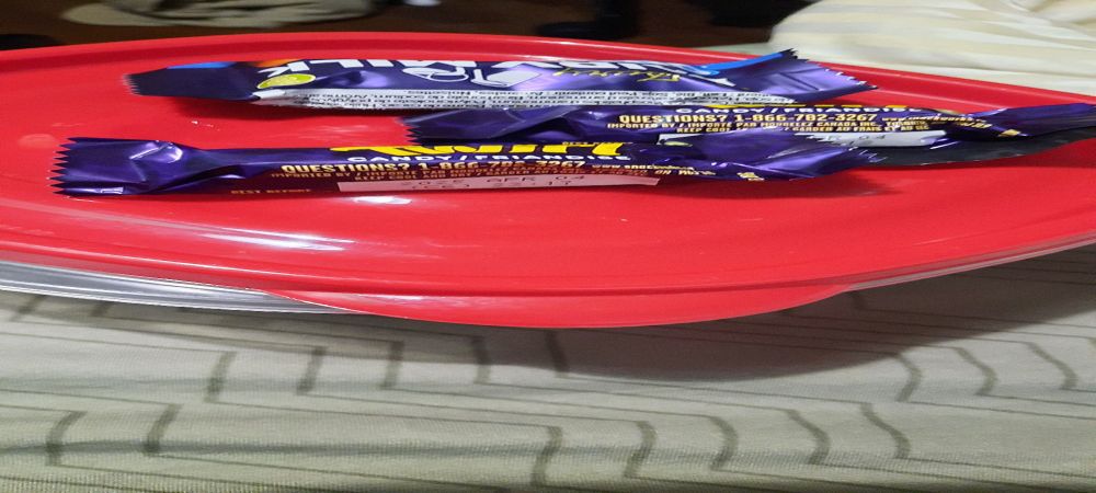 Three fun sized chocolate bars on top of a reusable container with a red lid on a bed