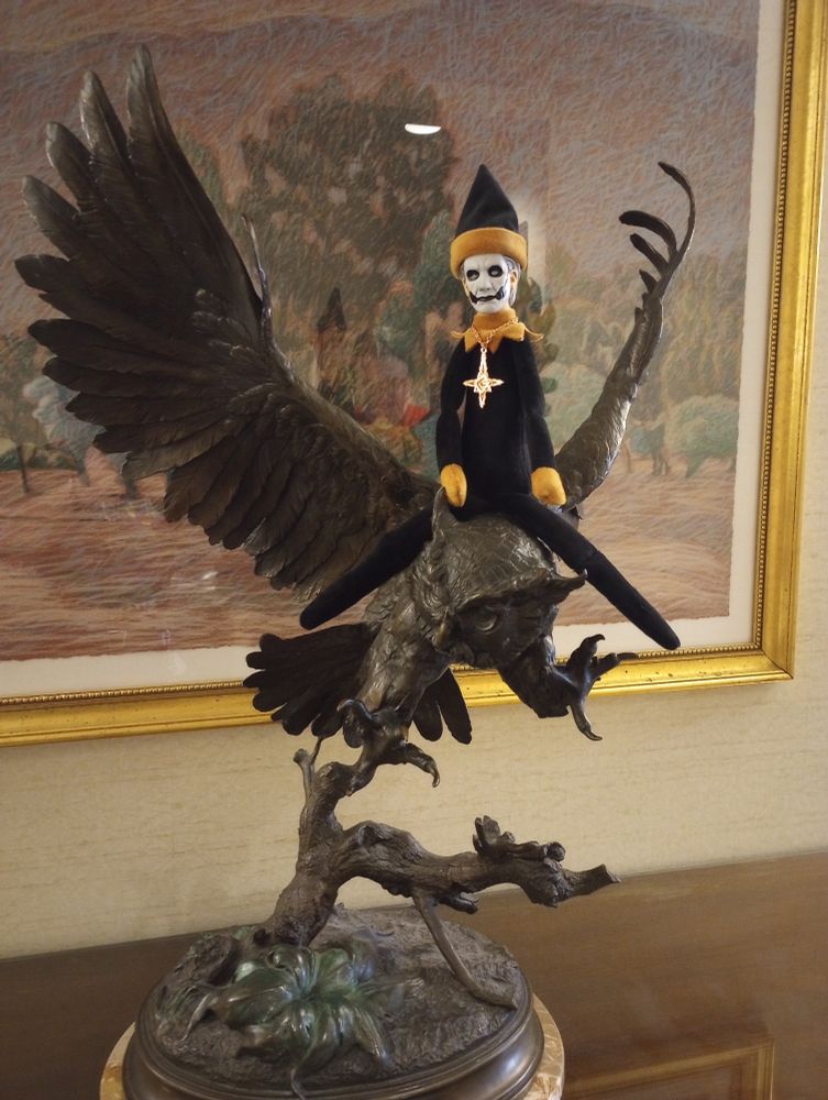 Image description, menace is writing a bronze statue of an owl. Behind him is a pointillism picture. This image is in a hotel hallway.