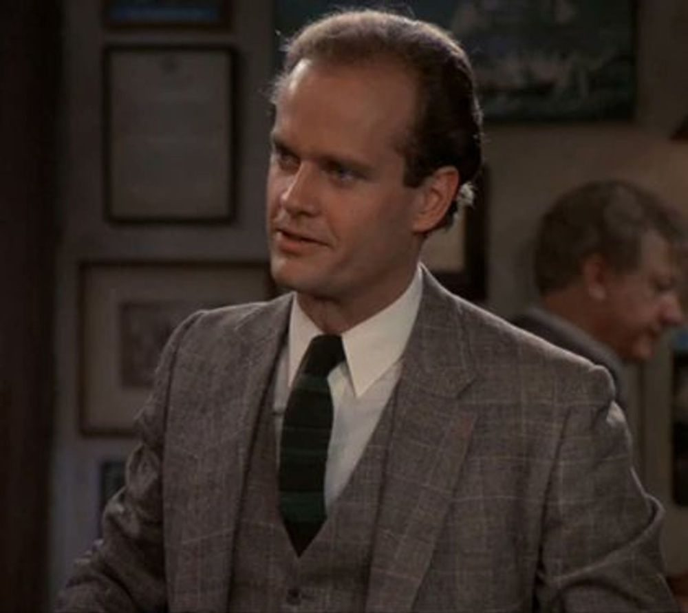 A color photo of the character Frasier Crane from the TV show Frasier, wearing a matching grey patterned suit jacket and vest, white shirt and dark patterned tie.