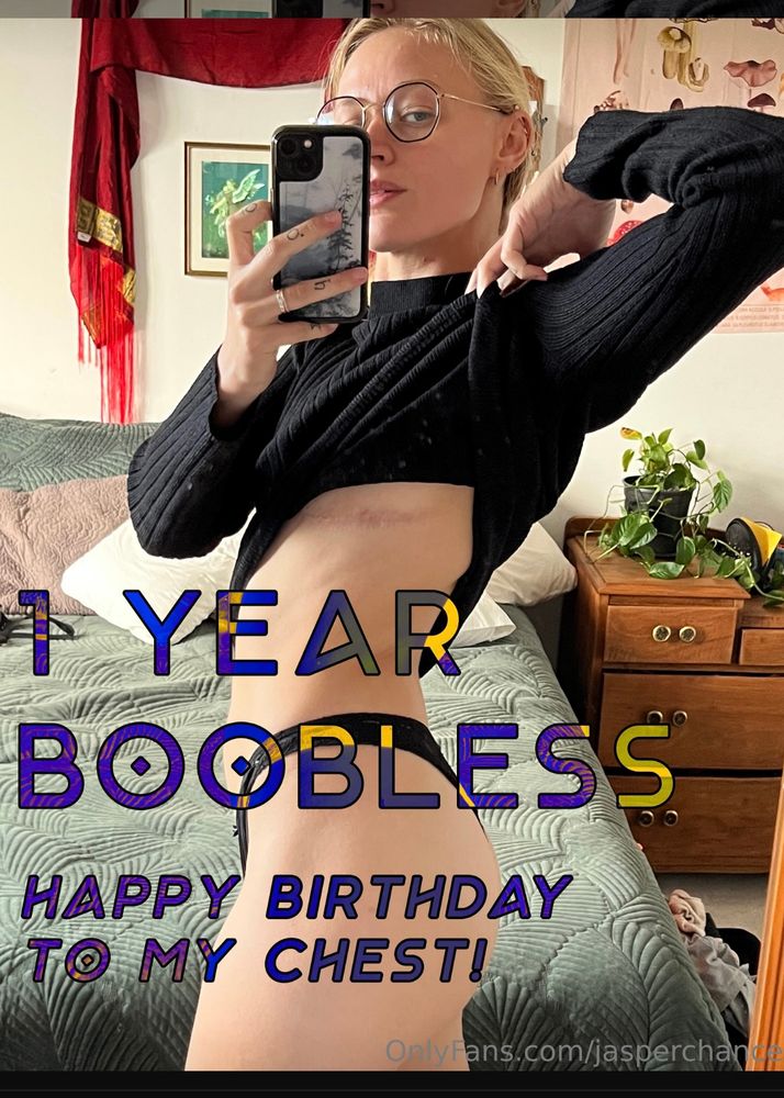 A selfie of Jasper from the side lifting their shirt up to reveal their top surgery scars. Text overlay says “1 year boobless! Happy birthday to my chest!”