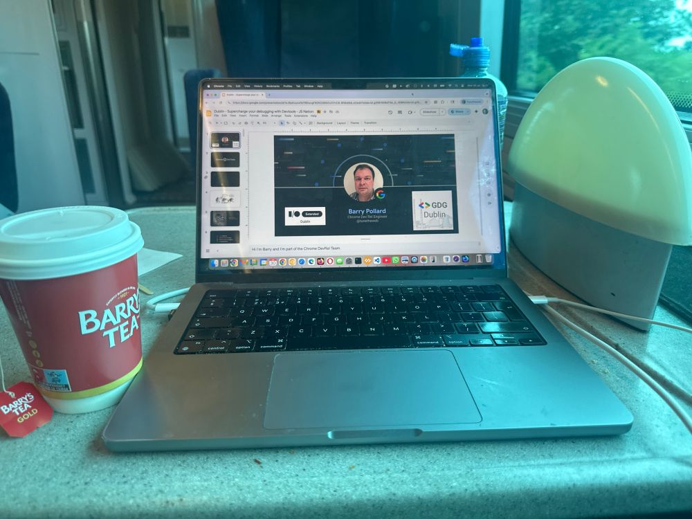 A laptop top with a slide deck, next to a cup of Barry’s tea.