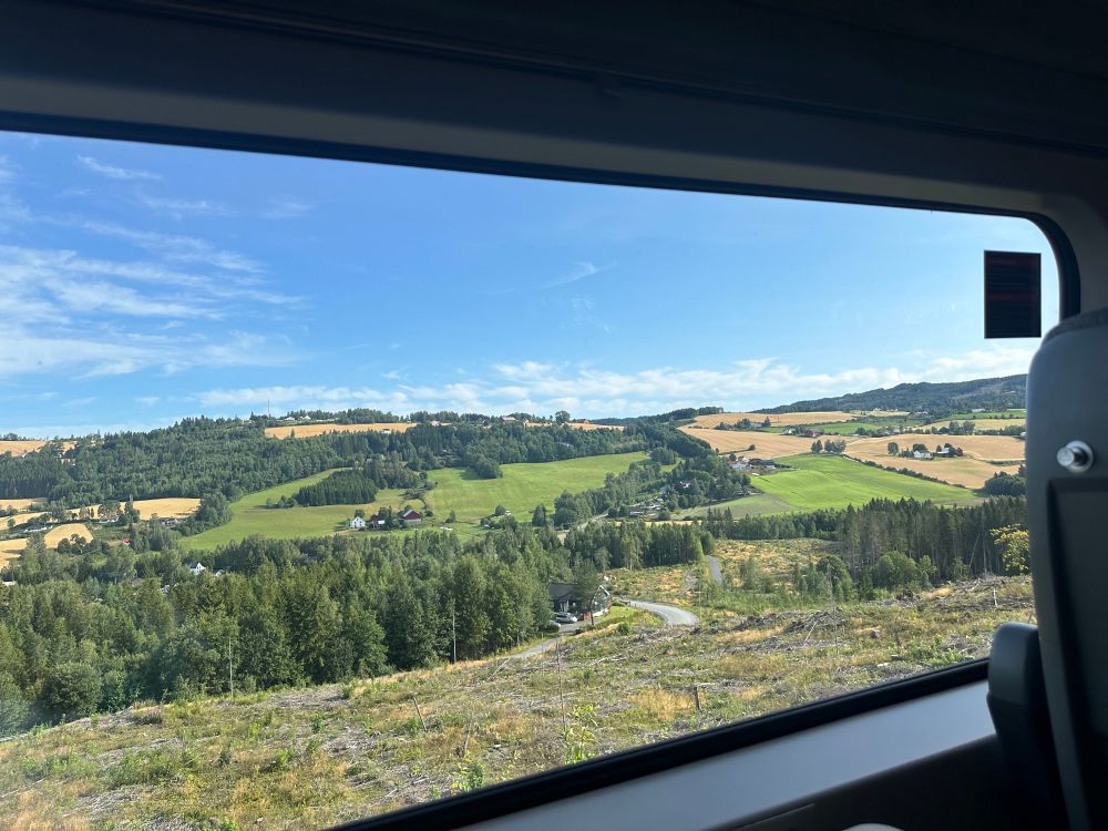 View of green fields under a blue sky framed by a train window.