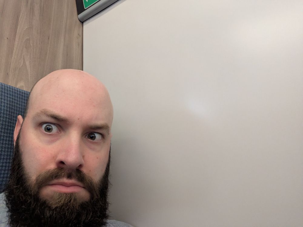 Matt sitting in a train seat advertised as a window seat, but with no window to look out of.