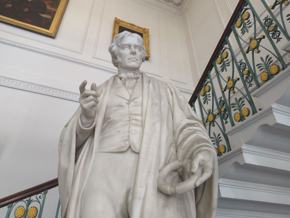 Michael Faraday's statue holding a coiled wire that looks a bit like a frisbee.