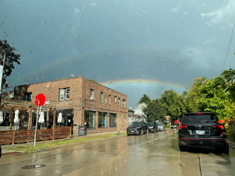 A photo of a reddish brown brick building in the bottom left with two rainbows over it