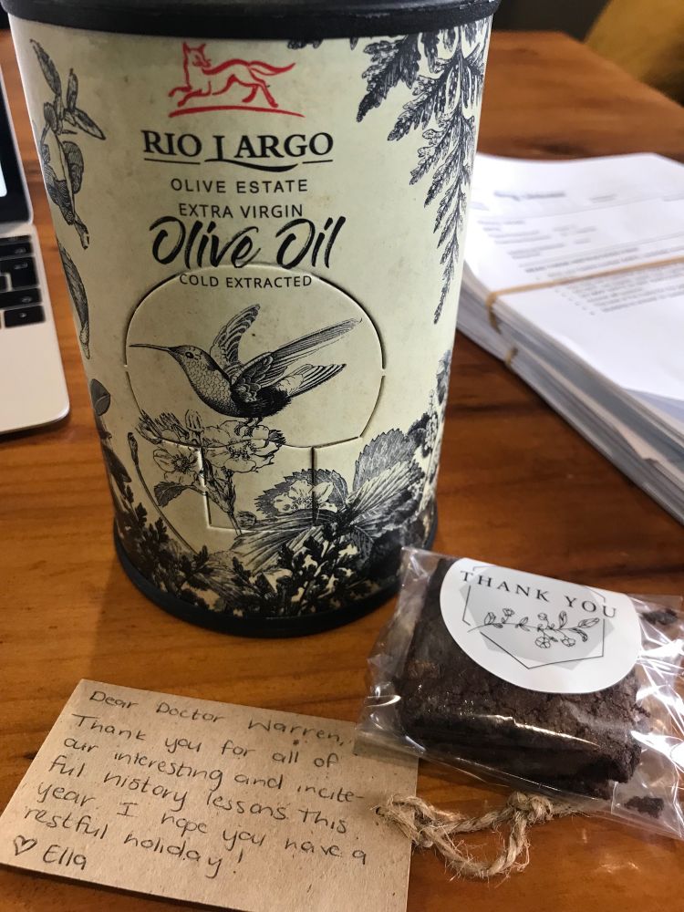 A bottle of olive oil, a brownie and a thank you note on a table. 