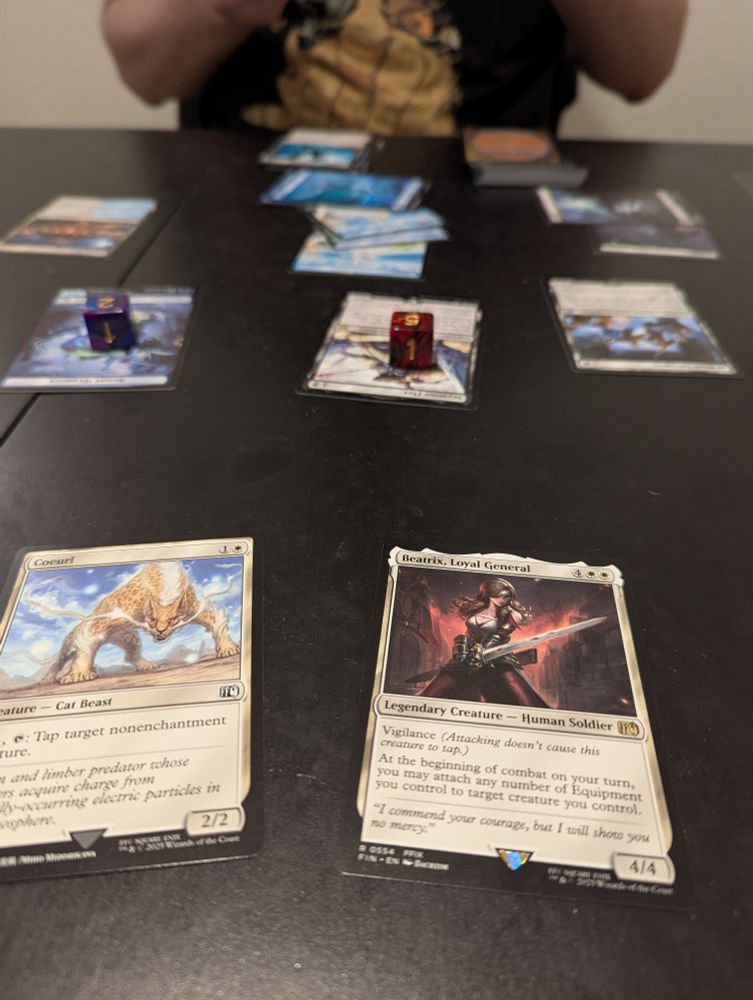 Closeup of a Coeurl and Beatrix card, my brothers cards (and my brother) are seen in the background.