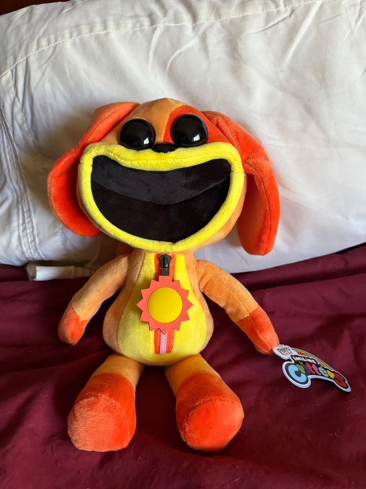 A plush of DogDay, the vanilla-scented orange canine leader of Playtime, Co.’s Smiling Critters toy line, sitting on my bed.