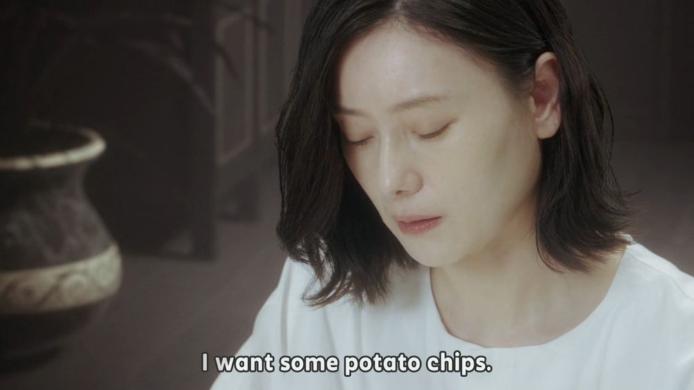 Screenshot from Kamen Rider Gavv of a flashback to the main protagonist, Inoue Shouma's, mother, as she's looking down at her out-of-frame plate of non-human food slop with a depressed face and a single tear as she bemoans "I want some potato chips."