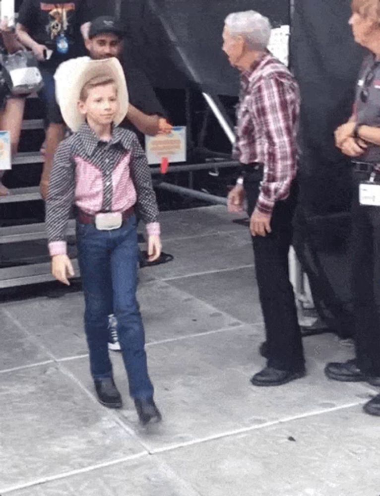 a young boy in a cowboy outfit is walking on a sidewalk