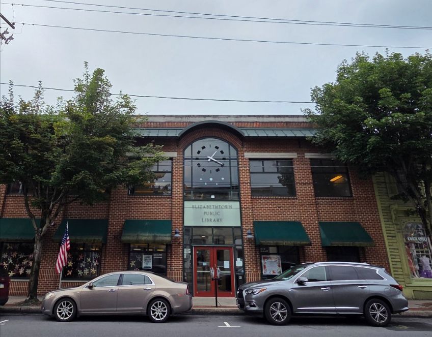 exterior of a brick library with two trees and two cars in front of it. 