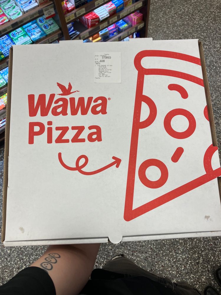 A white pizza box with red print. There is a picture of a slice of pizza and the text “Wawa Pizza”
