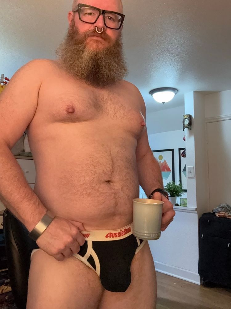 Bearded man in glasses wearing nothing but black briefs. 