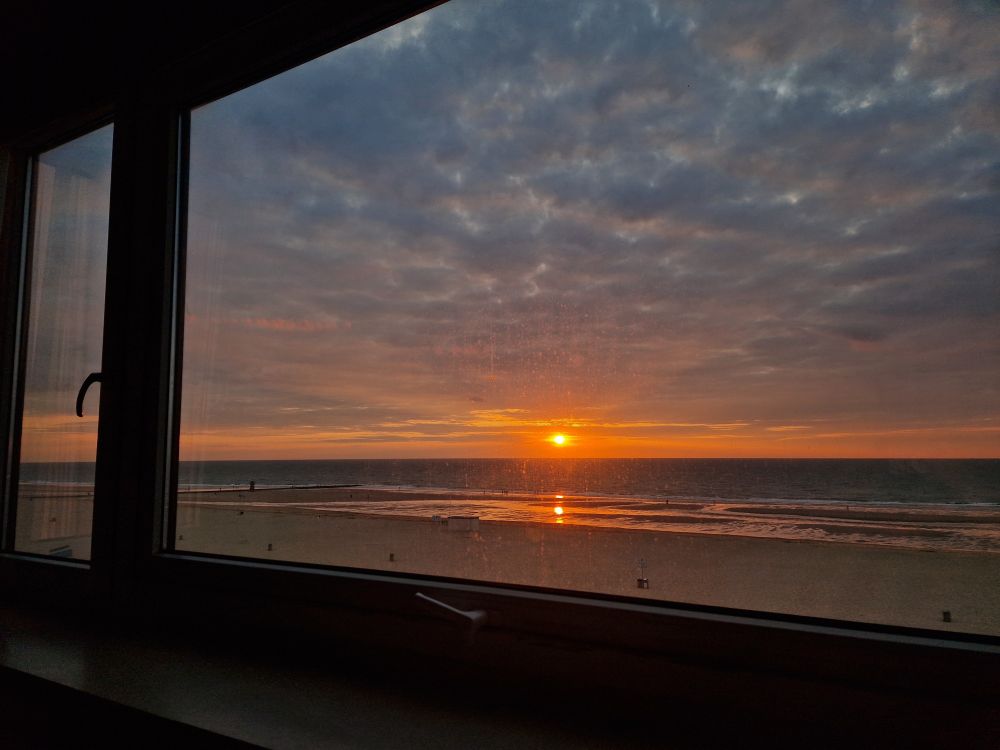 Sunset from the window of our holiday rental. Sun just above the sea, waves and a sandy beach with motled cloudy sky...