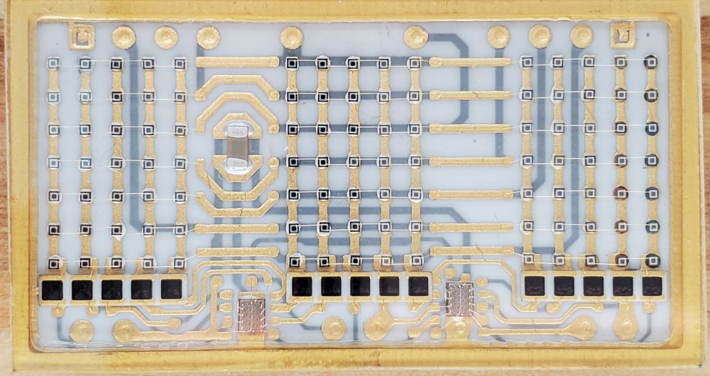 Top view of the ceramic module. The LED dies for each alphanumeric character are arranged in a 5x7 pattern. There are two IC dies at the bottom of the module. The black squares are possibly resistors. The dark grey rectangular object in the middle left of the module is a ceramic capacitor.