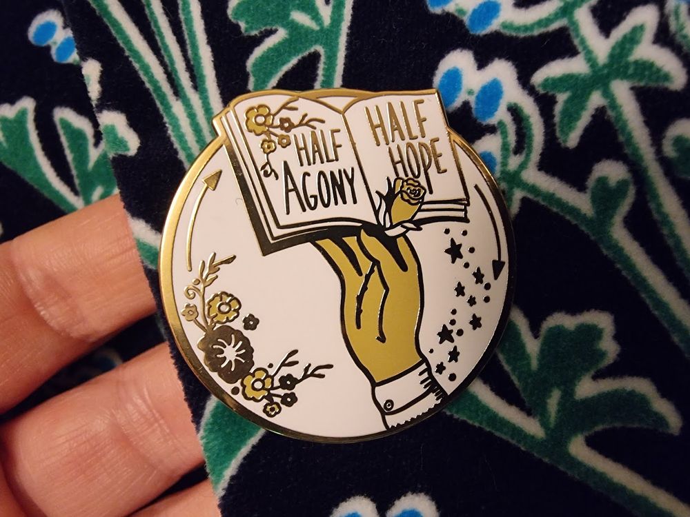 A pin badge on a lapel, with the words 'half agony / half hope'
