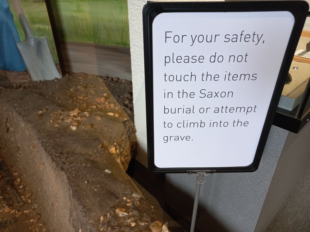 Museum display recreating a Saxon burial, with a notice reading:
For your safety, please do not touch the items in the Saxon burial or attempt to climb into the grave.
(Red House Museum, Christchurch)