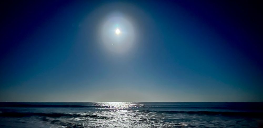 Moon rising above the ocean, its light reflected in the waves. 