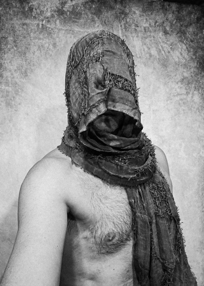 A black & white selfie of Mr. Otherbee from the abdomen up. He is adorned in naught but a rough fabric wrap that covers much of his face and hangs off of his left shoulder.