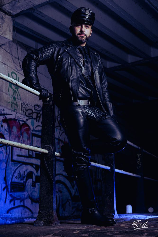 Man in full BLUF leather and boots posing against a railing.