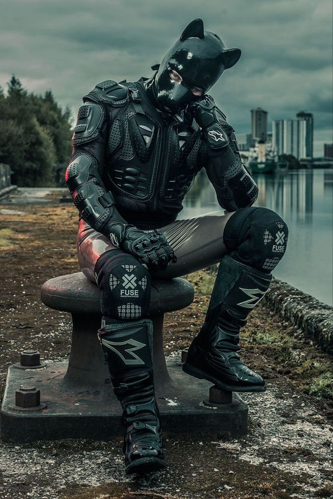Human pup sitting at a former port in rubber rand MX protective gear plus MX boots