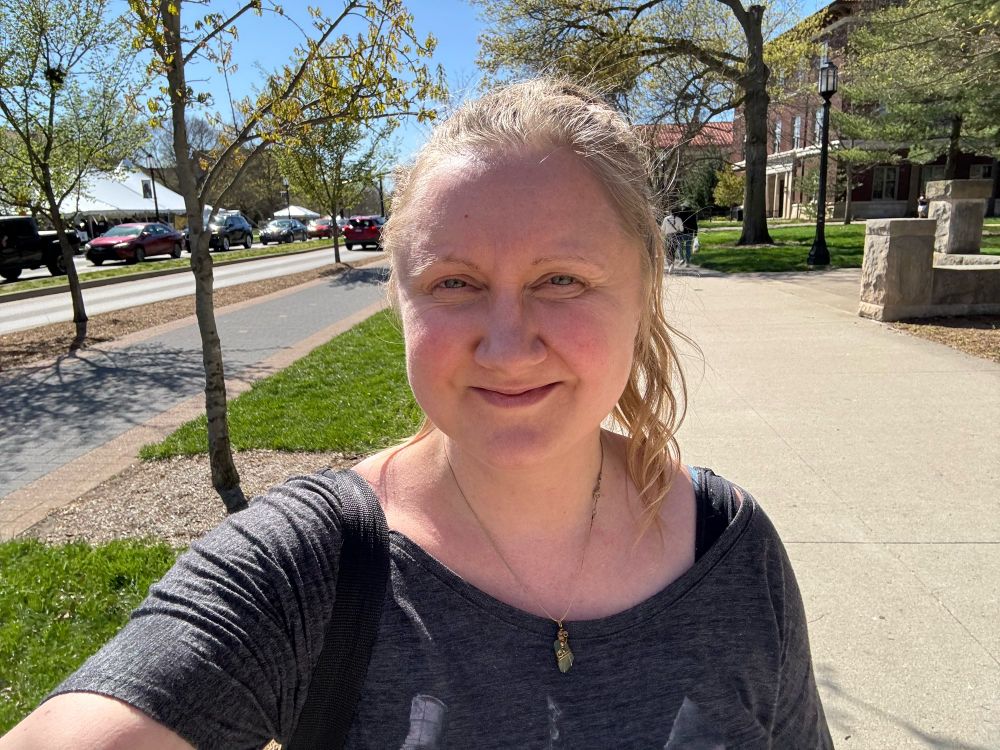 Selfie of Crystal in a gray shirt with a green sea glass pendant necklace and her blonde hair in a ponytail.