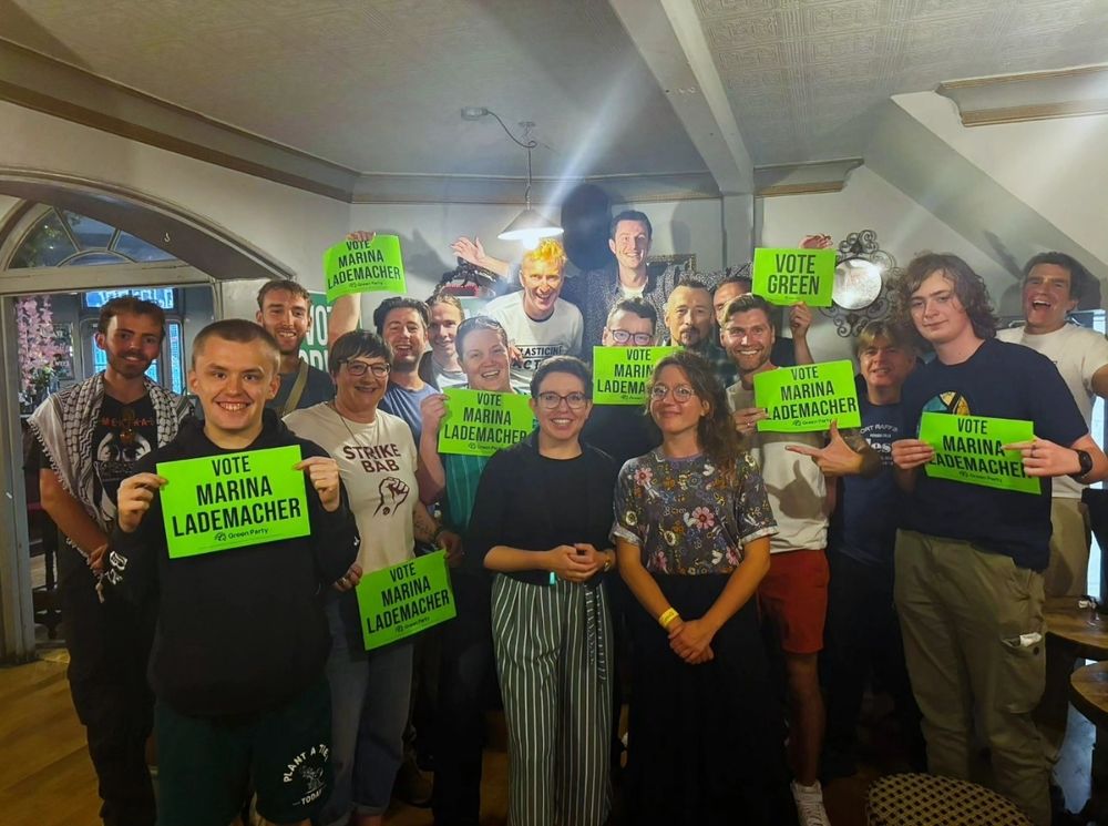 Carla Denyer, Marina Lademacher and Green campaigners posing with green vote Marina Lademacher signs in an indoor space