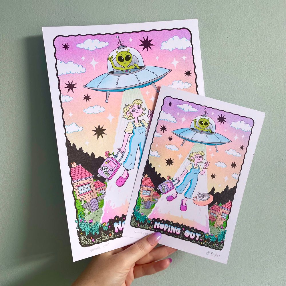 My hand holding two sizes of my new print - it’s a super colourful illustration of a lady getting abducted by a UFO. A smiley alien flys their saucer, and our lady floats up a beam of light carrying a packed bag and throwing a peace sign. Cat friend is also coming along. Text at the bottom reads “Noping Out”
