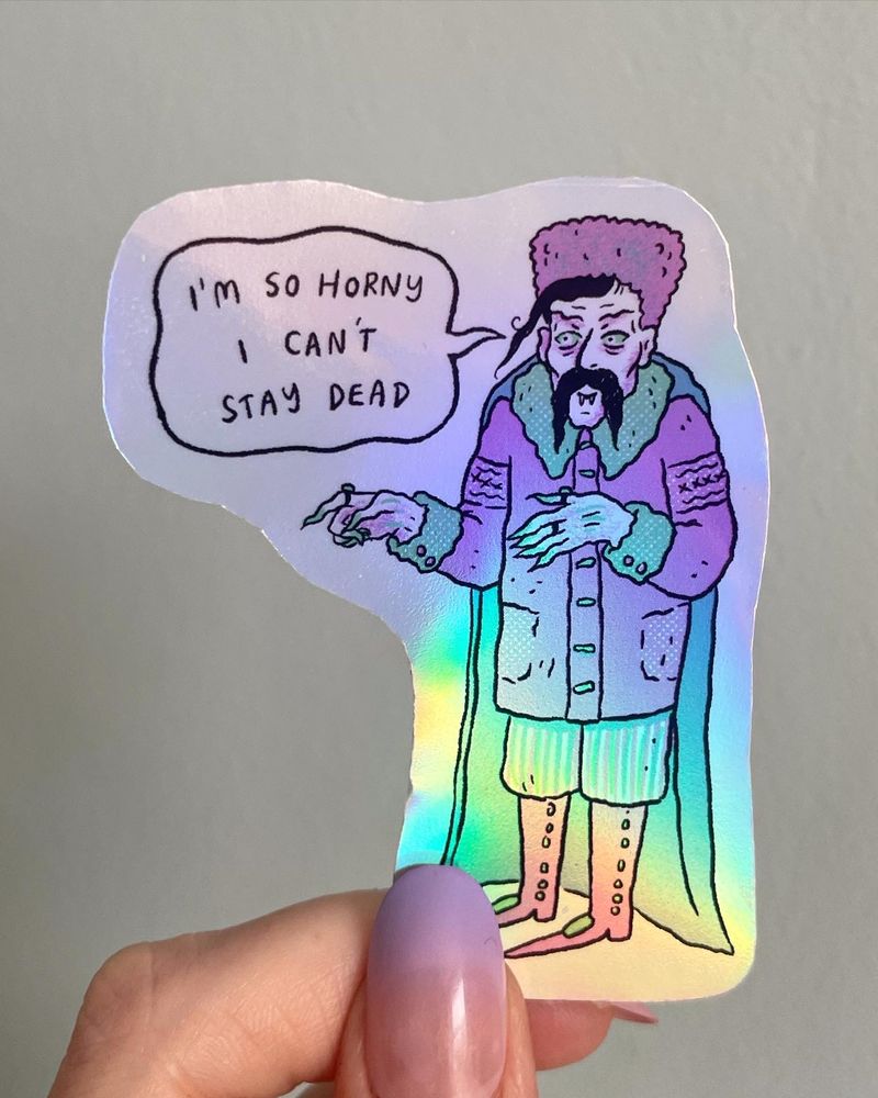Shiny holographic sticker with a cartoon drawing of Count Orlok from Nosferatu. He is saying “I’m so horny I can’t stay dead”