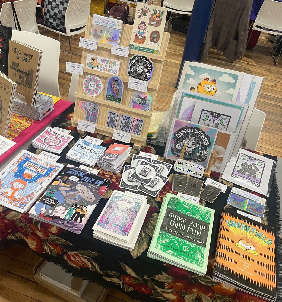 A table full of my comics, pin, stickers and prints. There’s a Garfield fan zine, a star steel zine and lots of illustrated guys spread out appealingly.