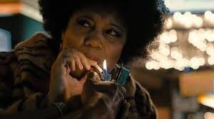 Woman with Afro in fur coat pulls on cigarette as it is being lit