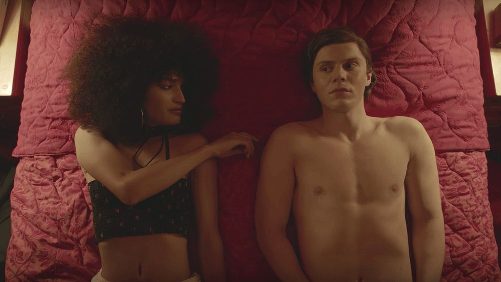 Woman with Afro poking the shoulder of a man laying next to her on a bed