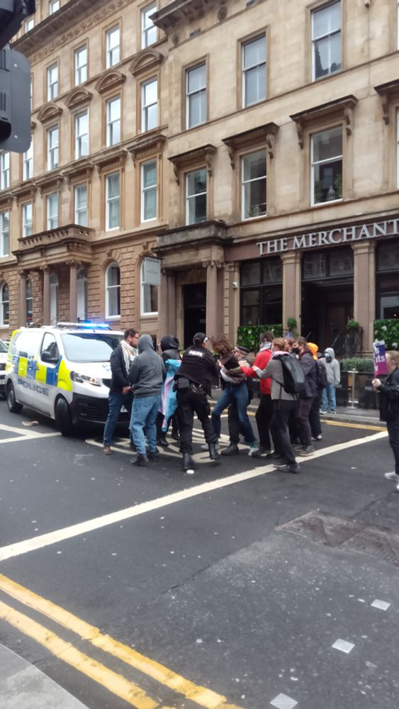 Protesters struggle with police in front of a van in the middle of the road.