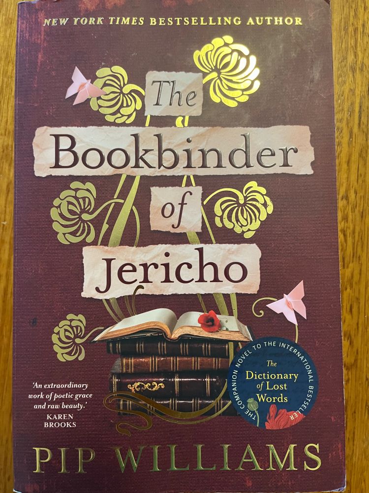 A picture of the cover of a maroon paperback book titled, The Bookbinder of Jericho, by Pip Williams 