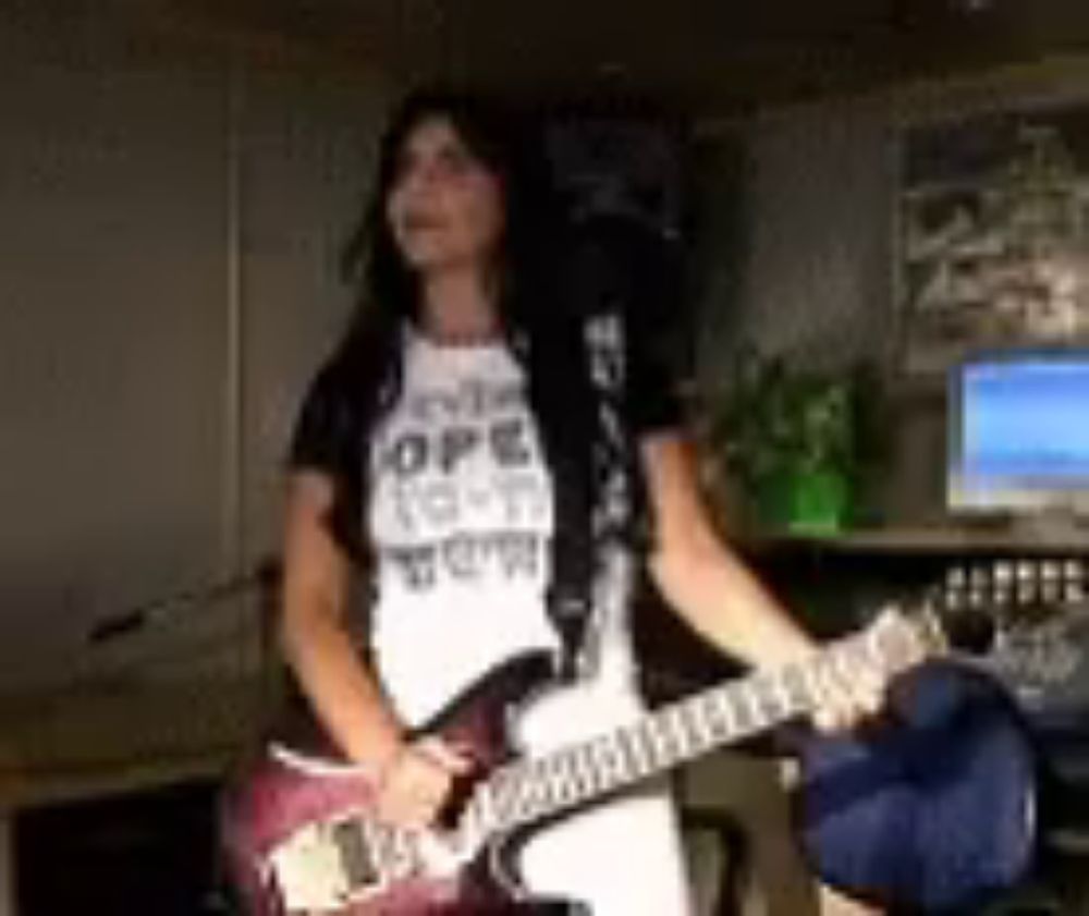 a woman in a white shirt is playing a guitar in front of a computer .