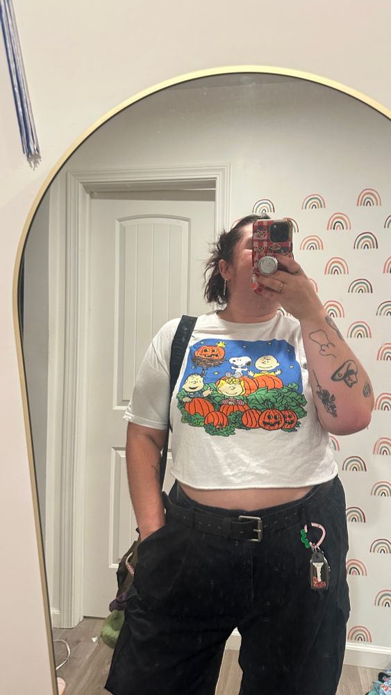 Katelyn in black pants and a Peanuts Halloween tshirt. Also holding their purse. 