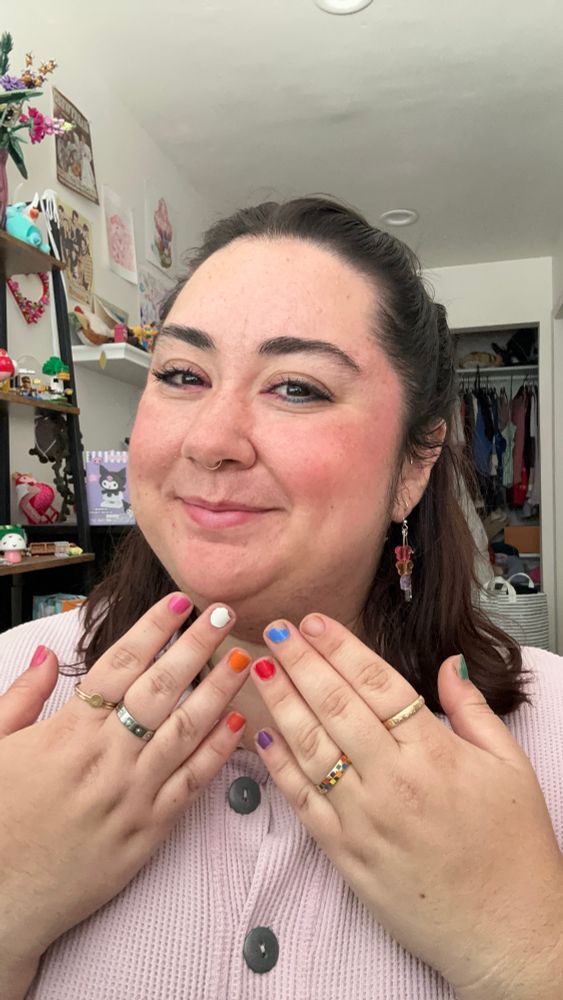 Katelyn holding up their hands and showing rainbow painted nails. 