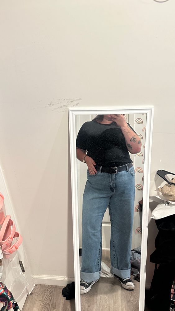 A photo of Katelyn in jeans and a black tshirt. They are also wearing converse and a black belt. 