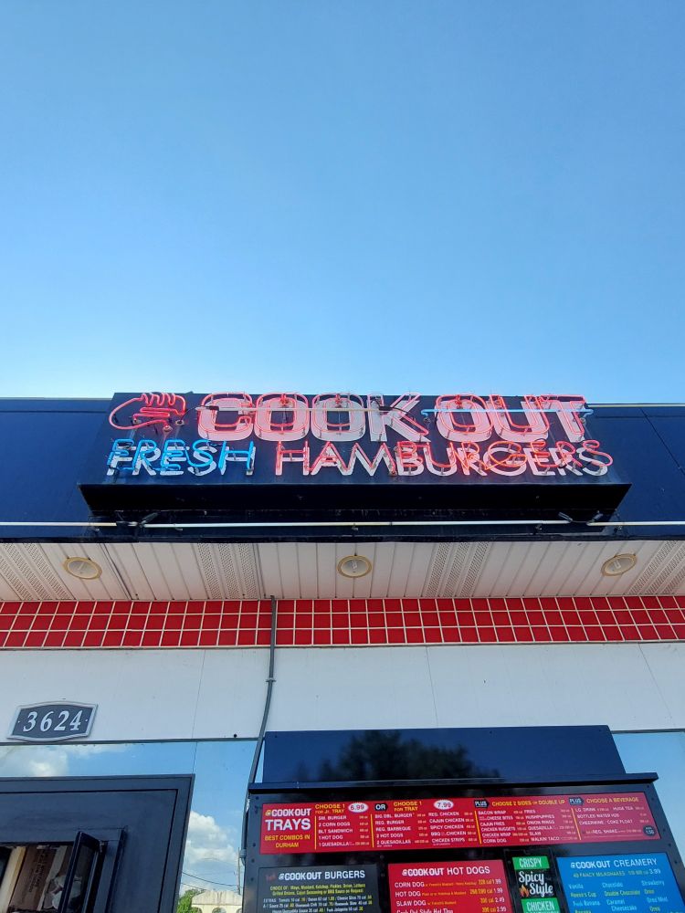 A photo of a neon sign for the chain restaurant COOK OUT that also says Fresh Hamburgers on top of a small building.