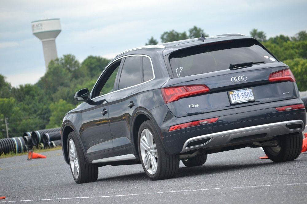 Photo of a navy blue Audi crossover driving quickly around a course in a parking lot.